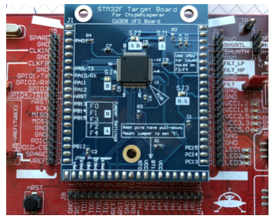 Фотография синей целевой платы STM32F, платы CW308 UFO, установленной на красной материнской плате. Плата предназначена для работы с ChipWhisperer для анализа побочных каналов.